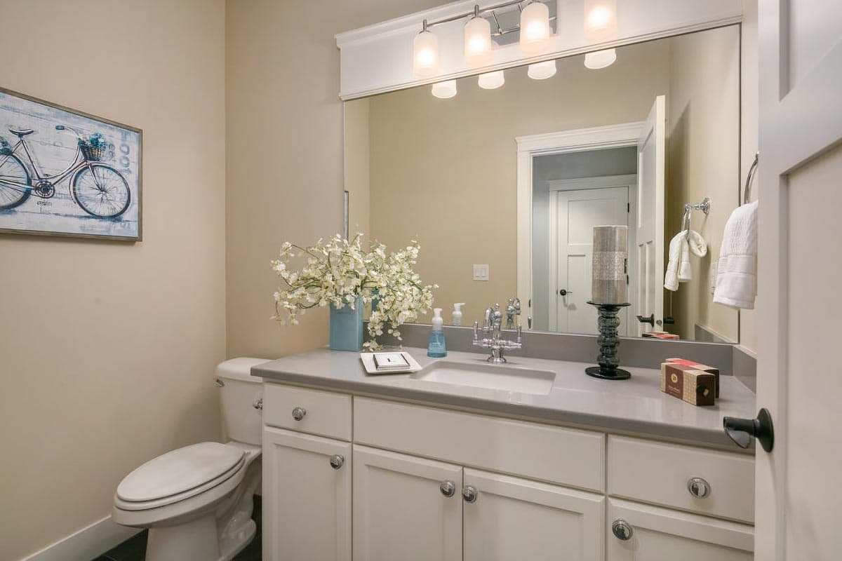 Bathroom vanity with double sink, toilet, and wall-mounted cabinet. Above vanity is large mirror and sconce lighting.