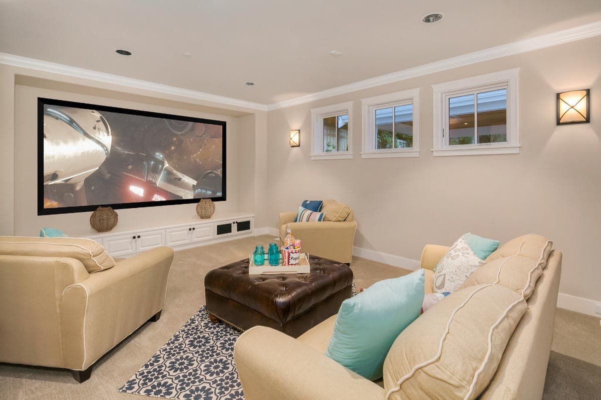 Home theater room with large projector screen, built-in cabinetry, comfortable seating, and three windows.