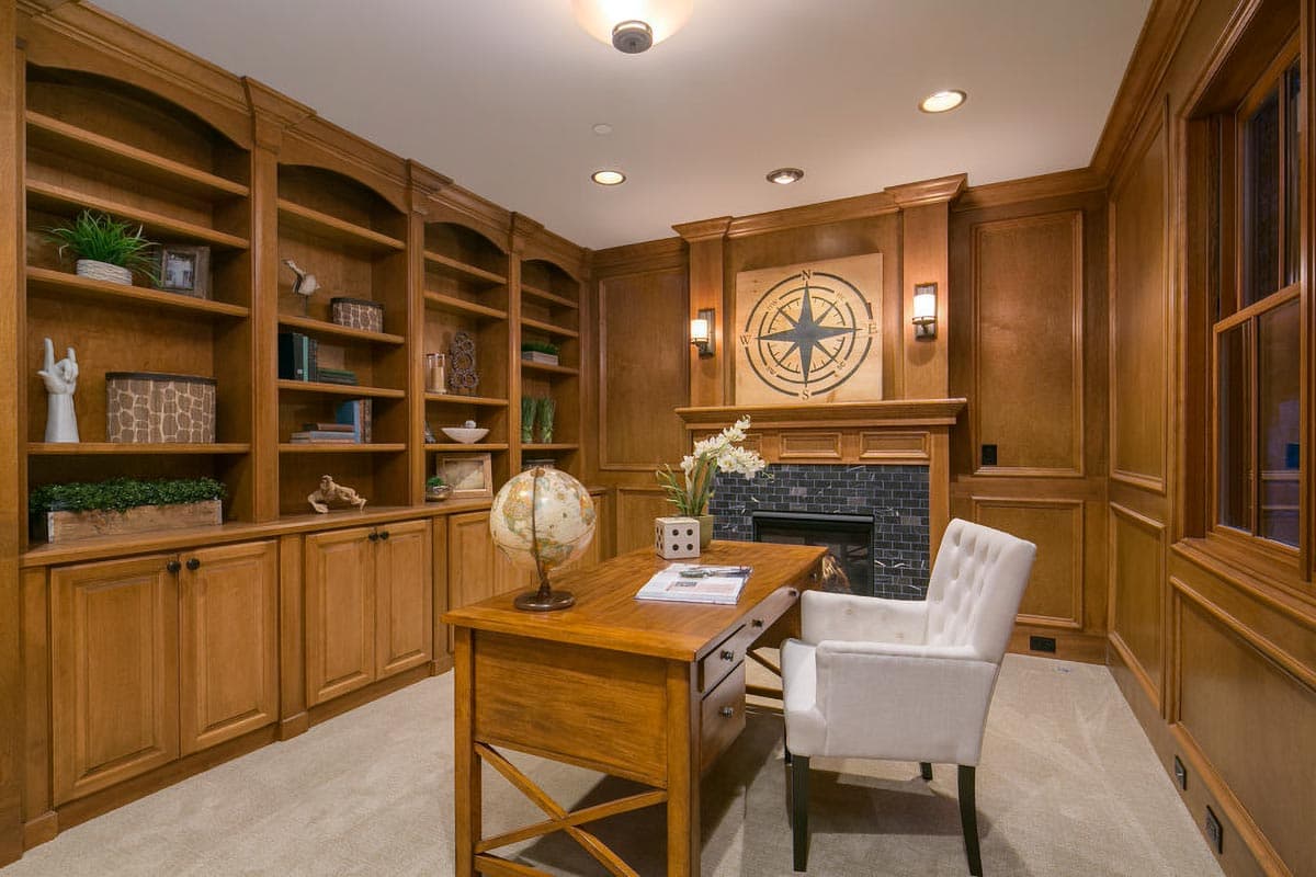 Study with built-in bookcases, fireplace with dark tile surround, wooden desk, and tufted chair.