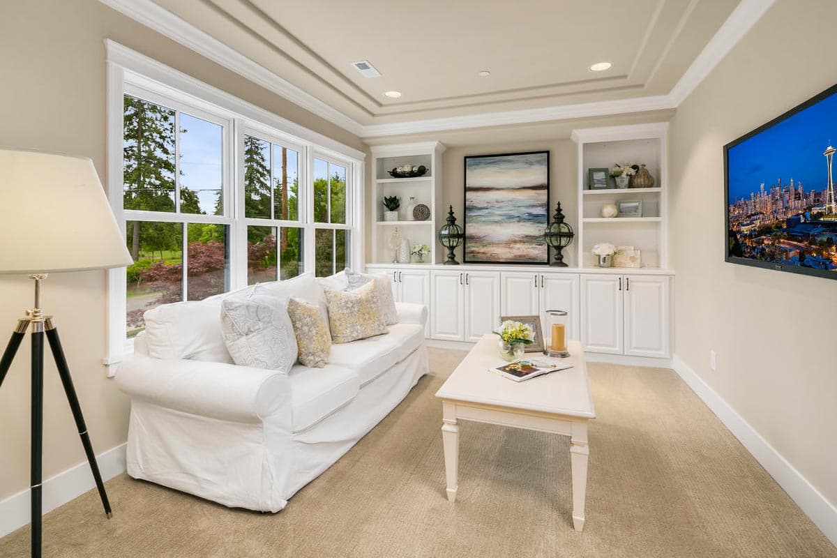 Living room with coffered ceiling, built-in white cabinets and shelves, sofa, coffee table, and large windows.