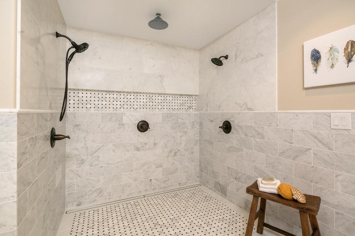 Marble tiled walk-in shower with multiple showerheads and decorative mosaic tile accent.