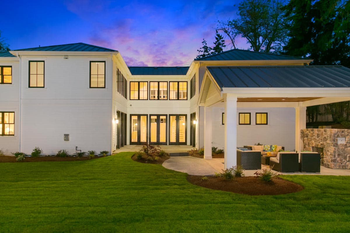 Modern house plan exterior with white siding, metal roof, multiple gables, and covered patio with stone fireplace.