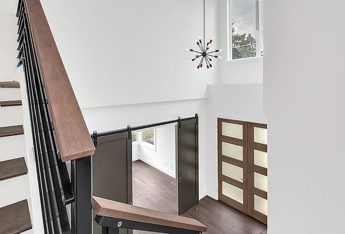 Interior view of a modern home featuring a floating staircase with dark wood treads, black metal railings, barn doors, and frosted glass double doors.