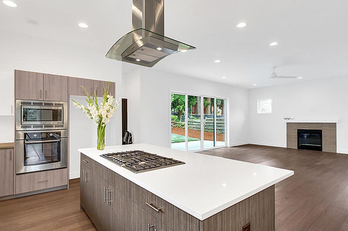 Modern kitchen with island gas range and stainless steel appliances, adjacent to open great room with fireplace.