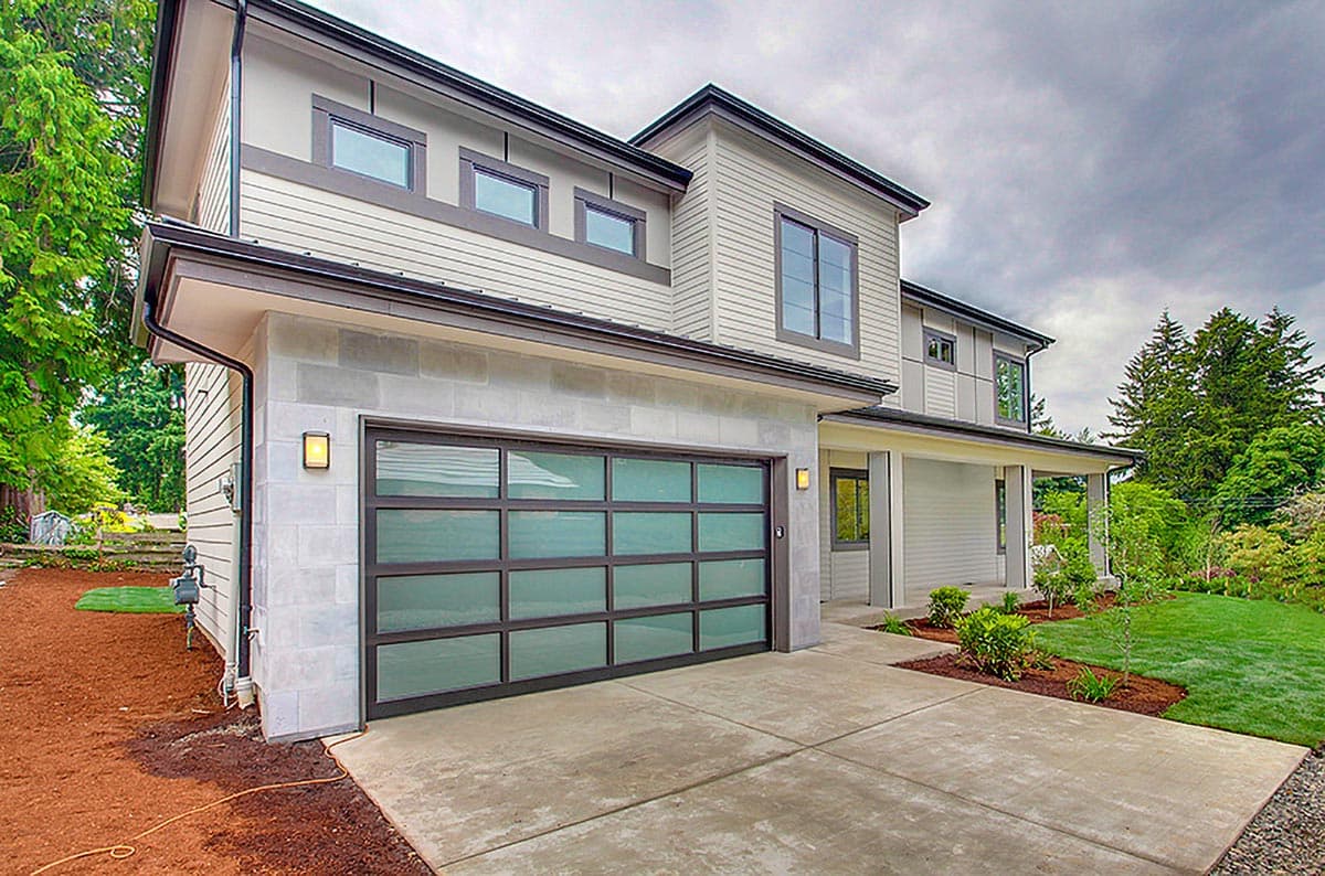 Modern two-story house exterior with a glass garage door, horizontal siding, and stone accents.