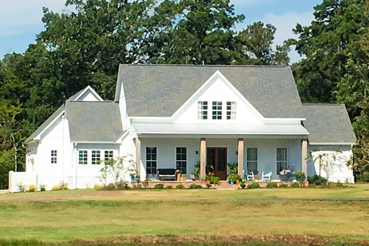 House plan exterior: Modern Farmhouse style, two stories, wide covered porch with columns, prominent gables, and varied rooflines.