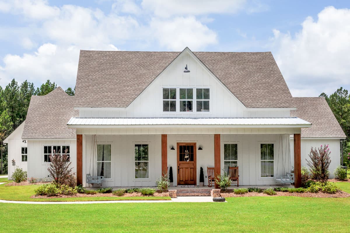House plan exterior. Farmhouse style, two-story home with a gabled roof and a covered front porch with exposed support beams. Features dormers.