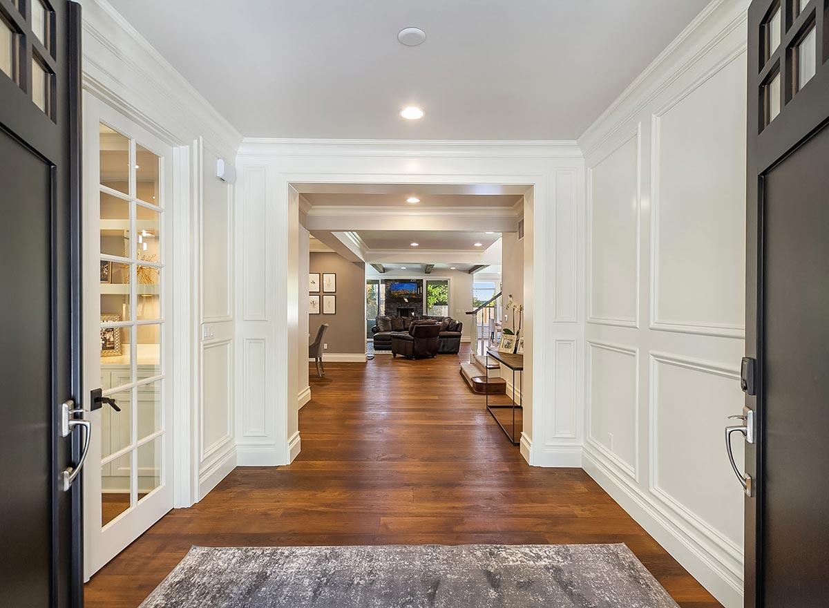 Interior view of a house entrance with French doors, wainscoting, and an open view to a living area with a fireplace.