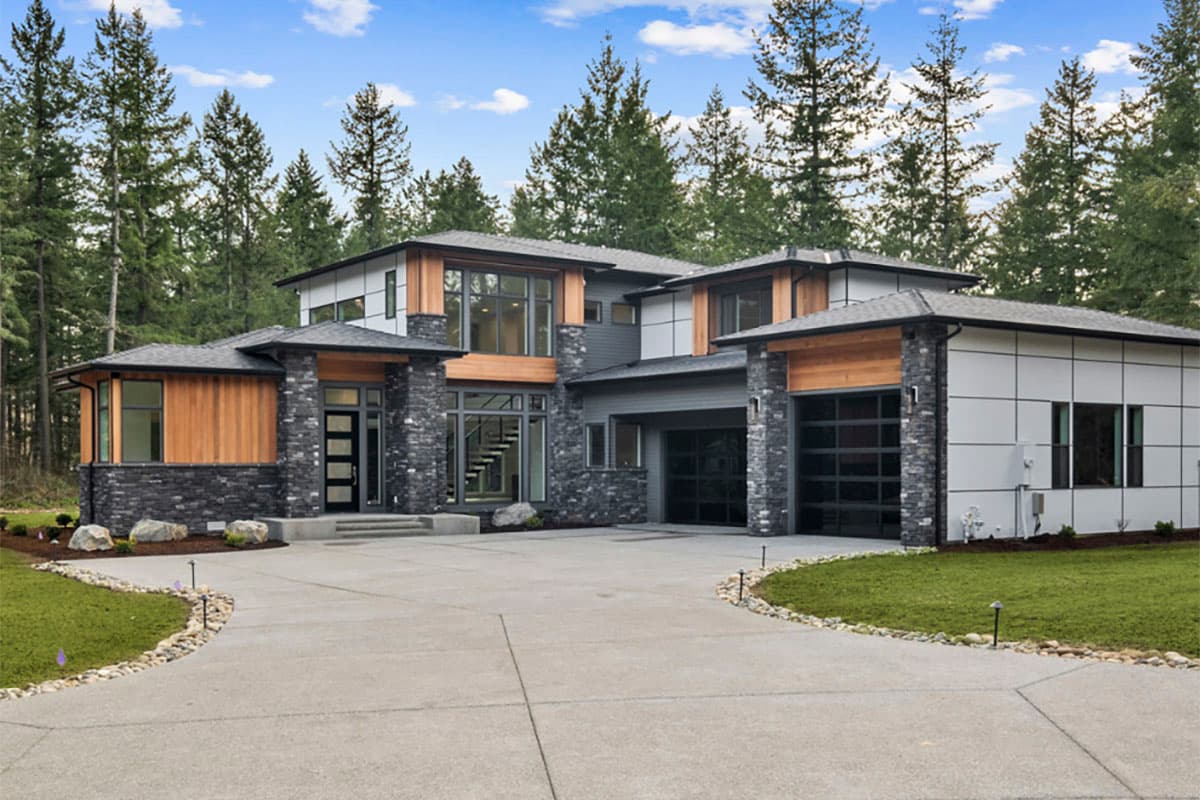 House plan exterior. Two-story modern style with flat rooflines, natural wood accents, and stone veneer. Features include a two-car garage.