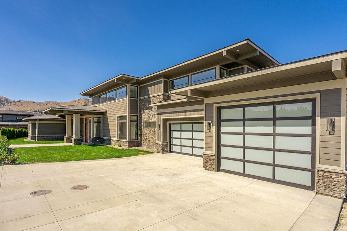 House plan exterior with two stories, wide overhangs, stone accents, and frosted glass garage doors.