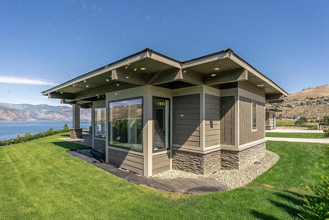 Modern house plan exterior with wide eaves, stone accents, and large corner windows overlooking a lake.