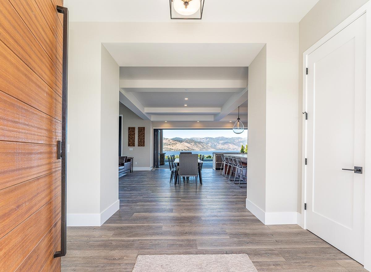 Interior view of a house with large open doorways leading to dining, kitchen, and living areas, featuring a wood front door and white interior doors.