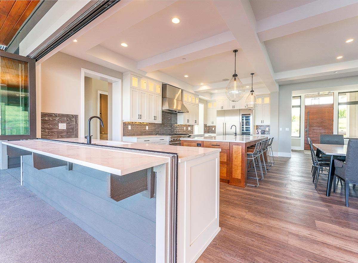 Modern kitchen with white cabinets, a large island, stainless steel appliances, and bi-fold doors opening to an outdoor area.
