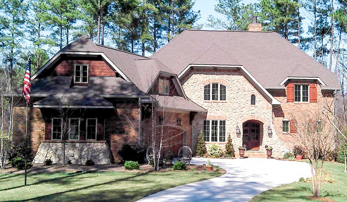 House plan exterior featuring brick and stone facade, multiple gables, arched entry, dormers, and a prominent roofline with asphalt shingles.