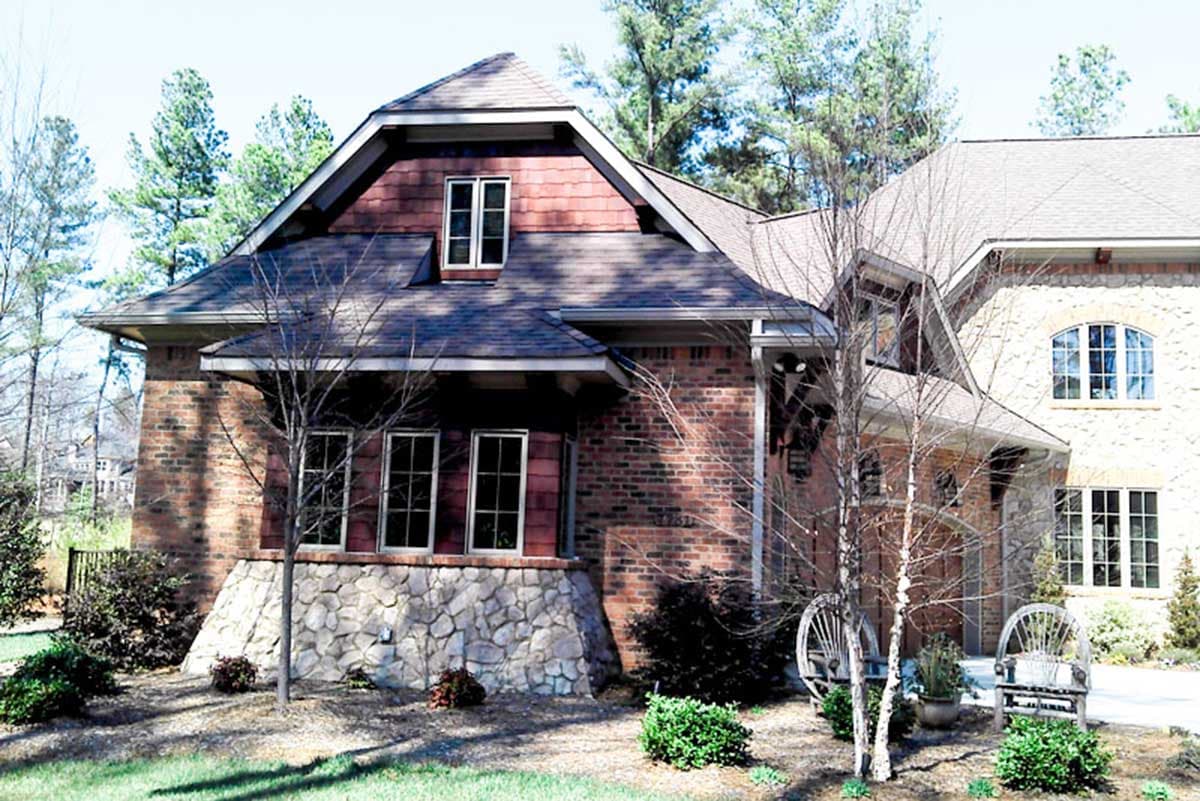 House plan exterior: Two-story brick and stone home with multiple gables, dormers, and a covered entry.