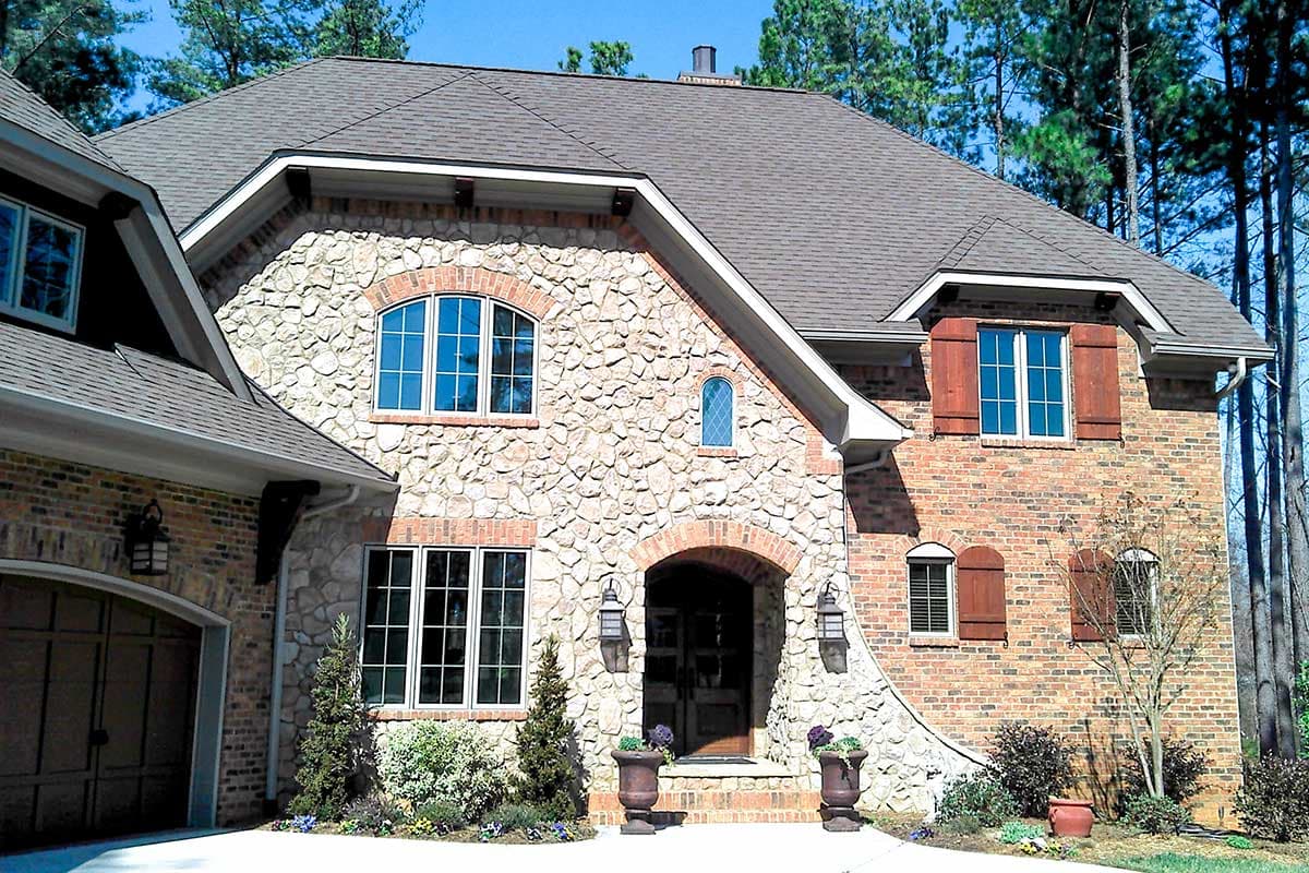 House plan exterior with stone facade, arched entry, gabled dormers, and attached garage.