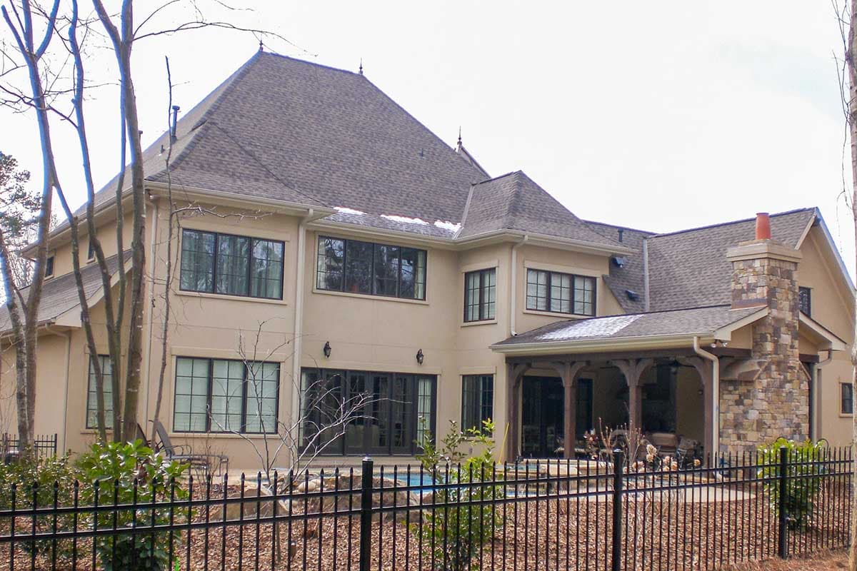 House plan exterior: Two-story home with multiple gables, stone chimney, covered porch, and large windows.