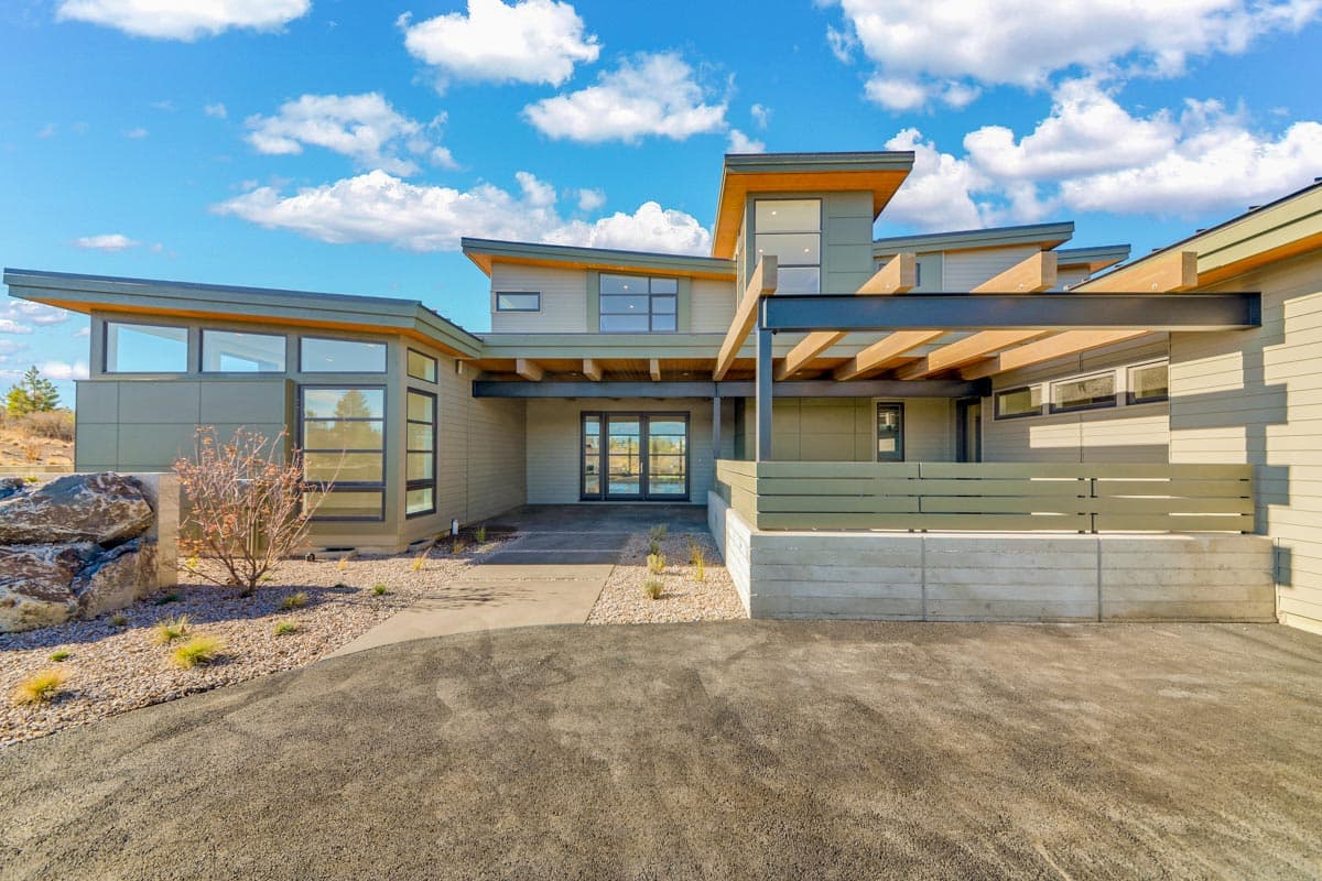 Modern house plan exterior with cantilevered rooflines, large windows, wood beam pergola, and concrete retaining wall.