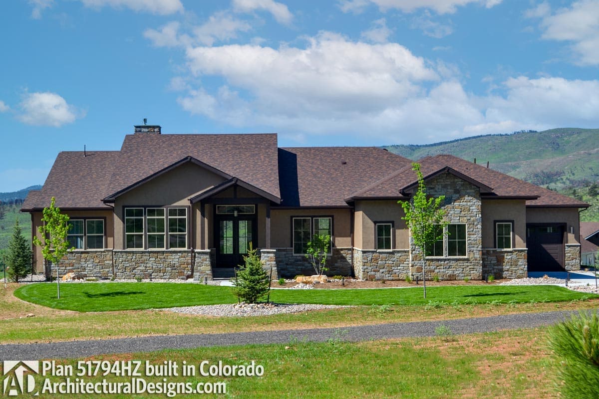 House plan exterior: One-story home with stone accents, prominent gables, and a covered entry with double doors.