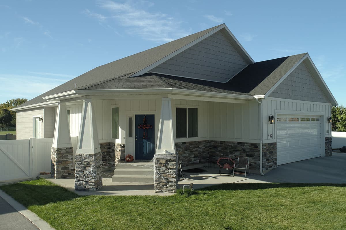 House plan exterior: Single-story home with stone accents, covered porch supported by stone-clad columns, and a two-car garage.