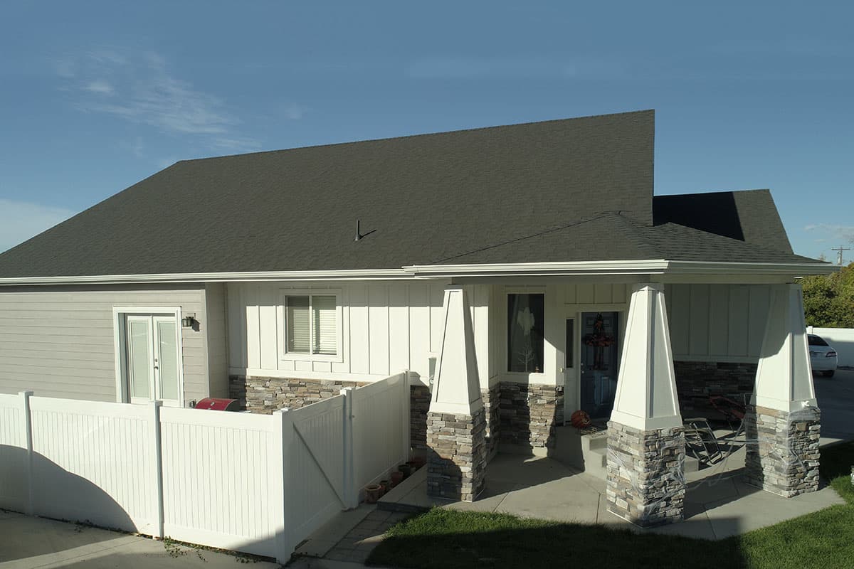 House plan exterior: One-story modern home with stone and board-and-batten siding, covered entry with stone-clad columns, and white vinyl fencing.