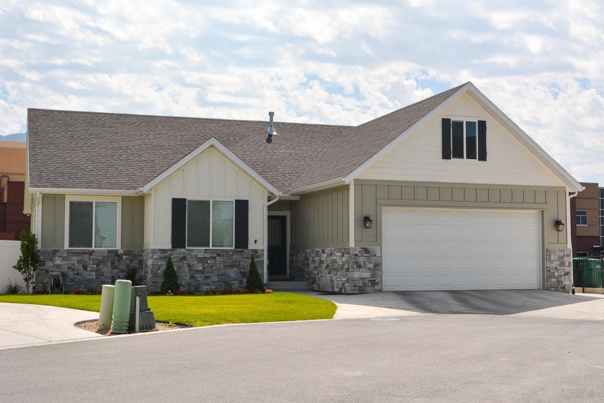 House plan exterior. Ranch style with stone accents. Features include gabled roof, garage, and vertical siding. Two stories.