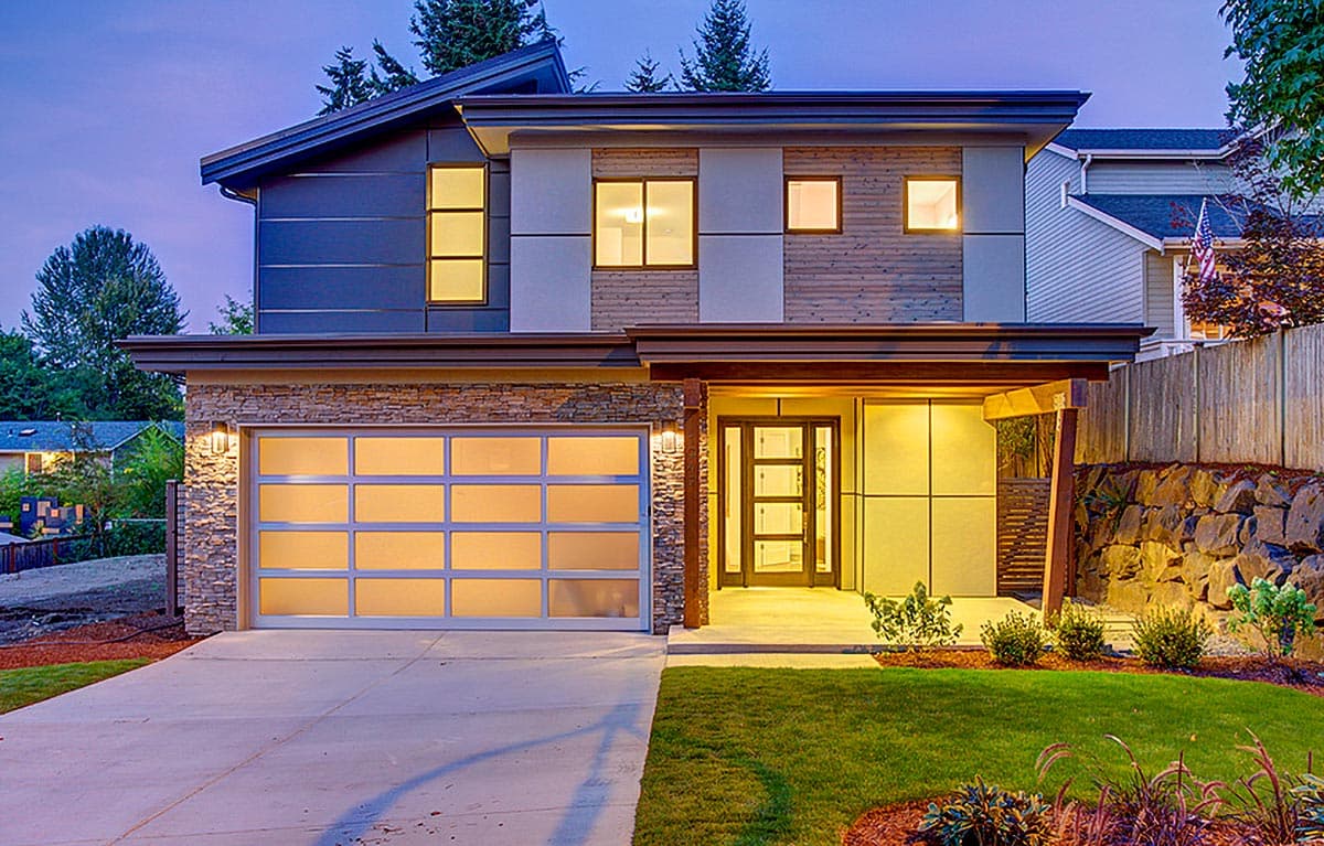 Modern house exterior with stone facade, contemporary rooflines, multiple window styles, and glass garage door.