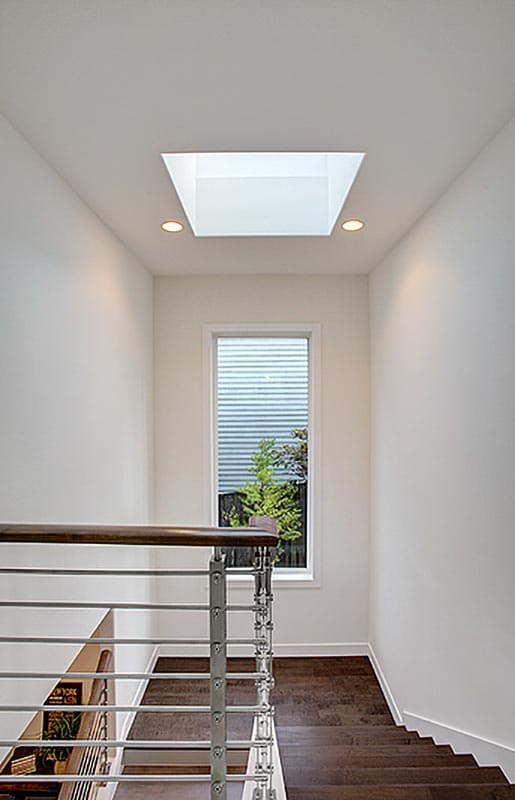 Interior stairway with skylight, vertical window, and modern metal railing with wooden handrail.