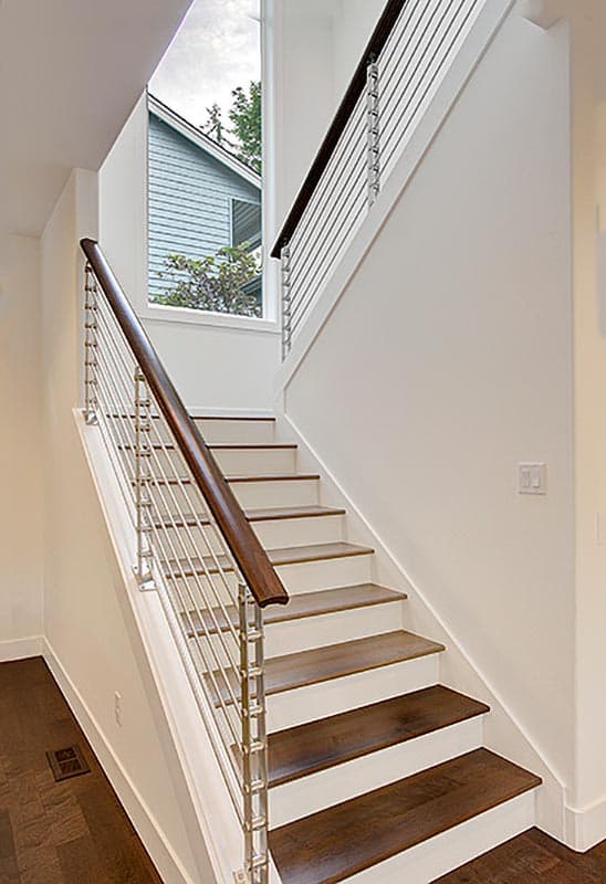 Interior view of a staircase with wood treads, open risers, and cable railing, featuring a tall triangular window.