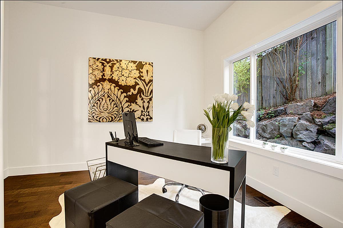 Office with modern desk, computer, seating, artwork, and large window overlooking rocky landscape.