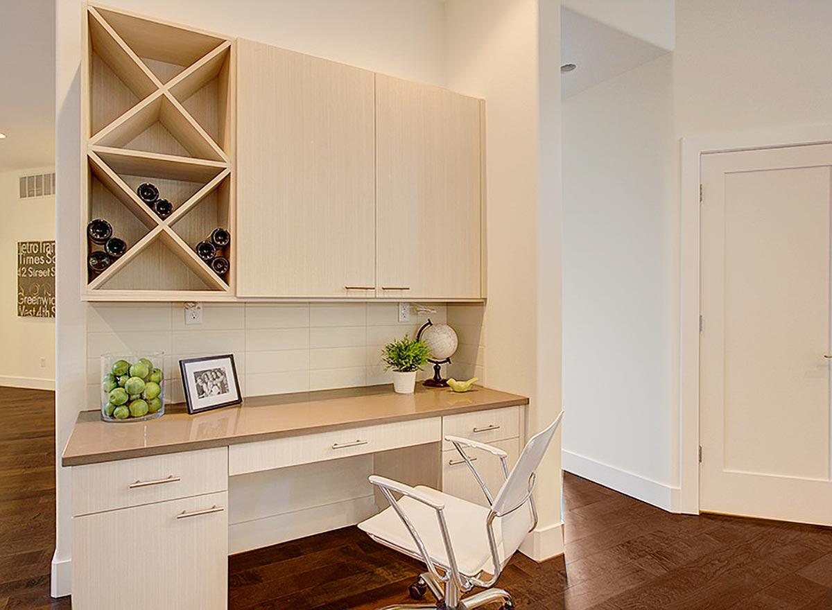 Interior view of a built-in desk with light wood cabinets, diamond wine rack, and rolling chair.