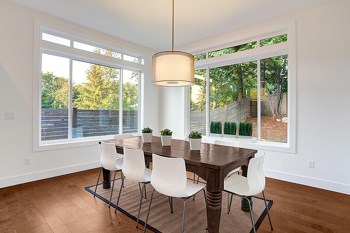 Dining room with large windows, dark wood table, and white chairs.