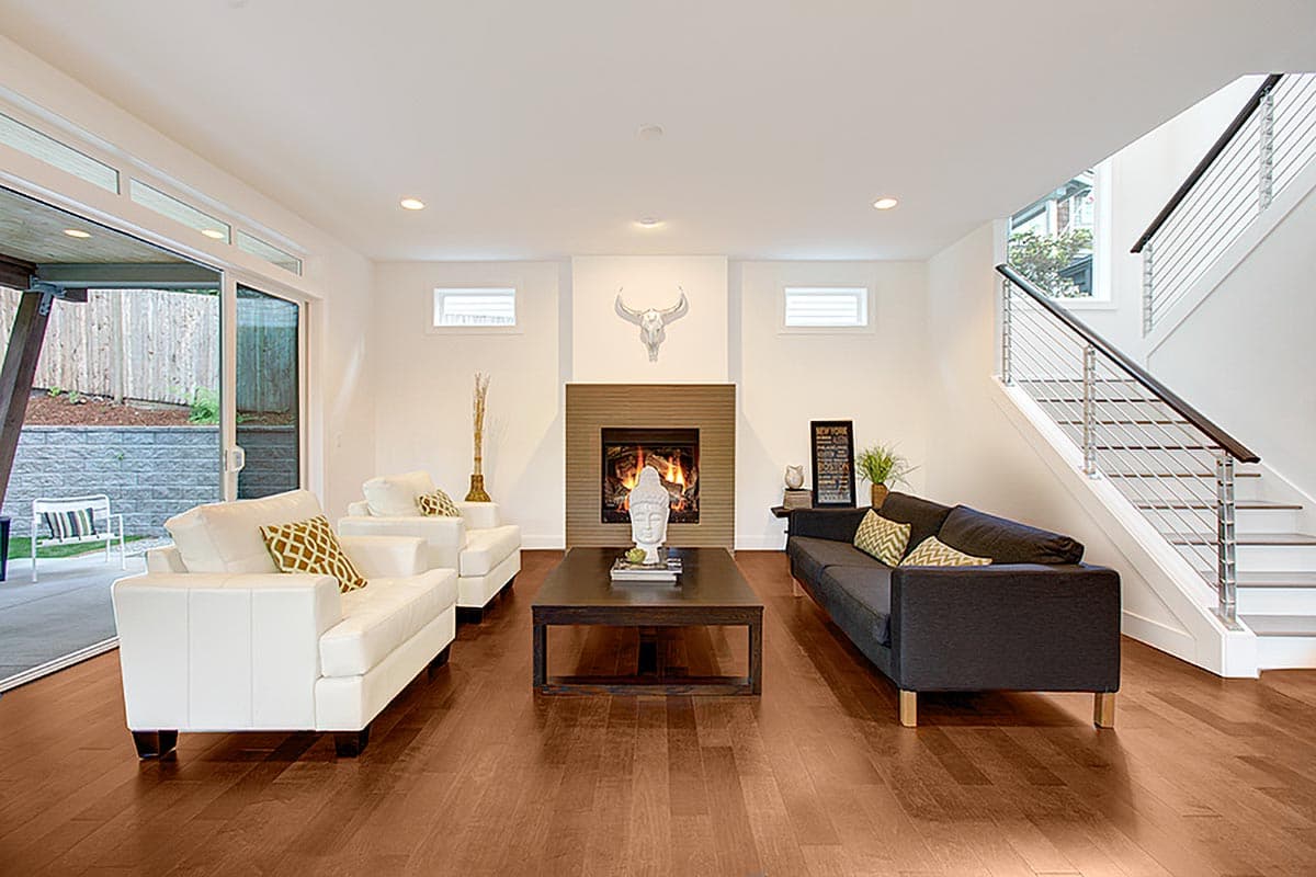 Modern living room with fireplace, white sofas, dark sofa, and open staircase with metal railing.