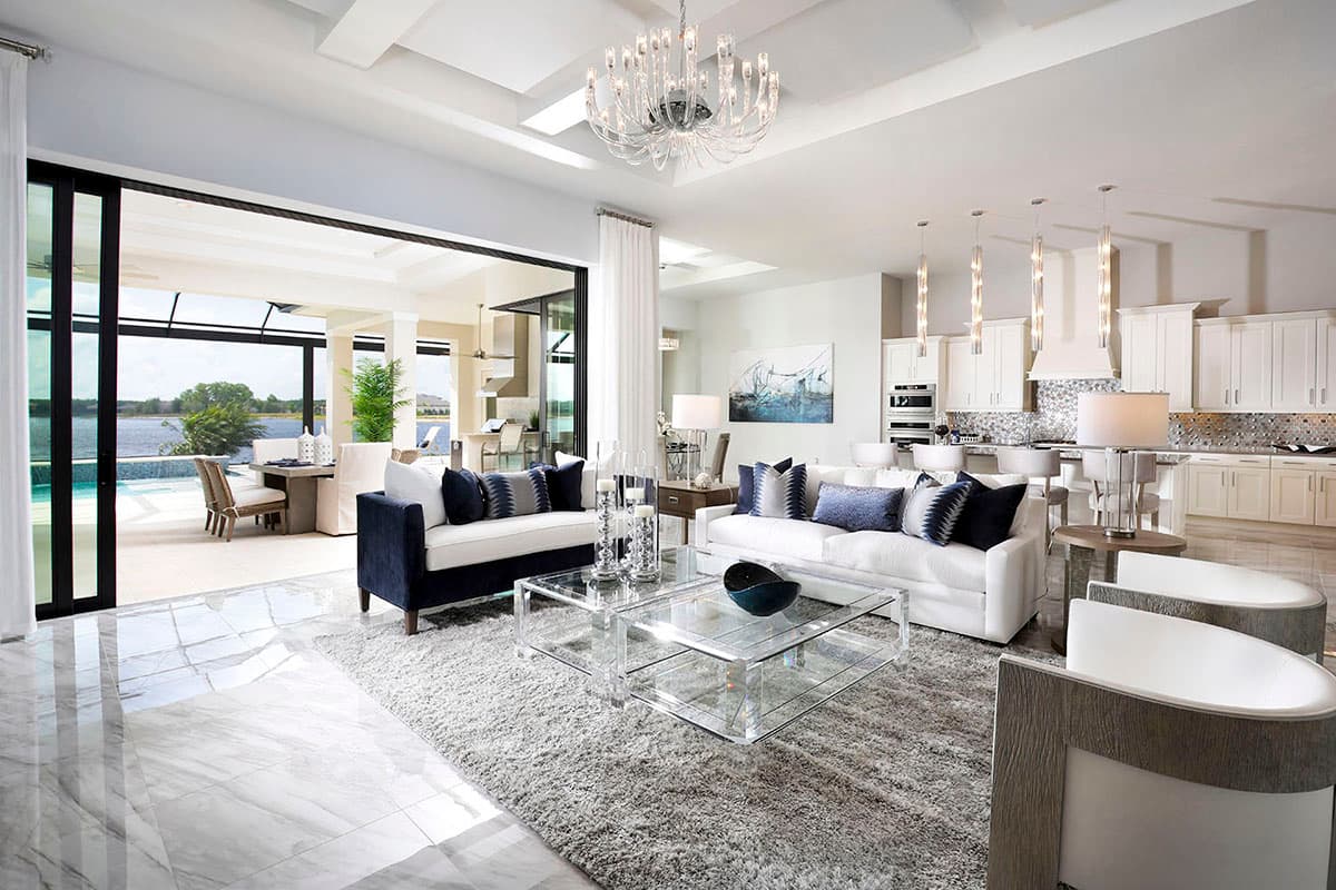 Open concept living area with sofas, glass coffee table, and kitchen island. Large sliding doors open to an outdoor patio and pool.