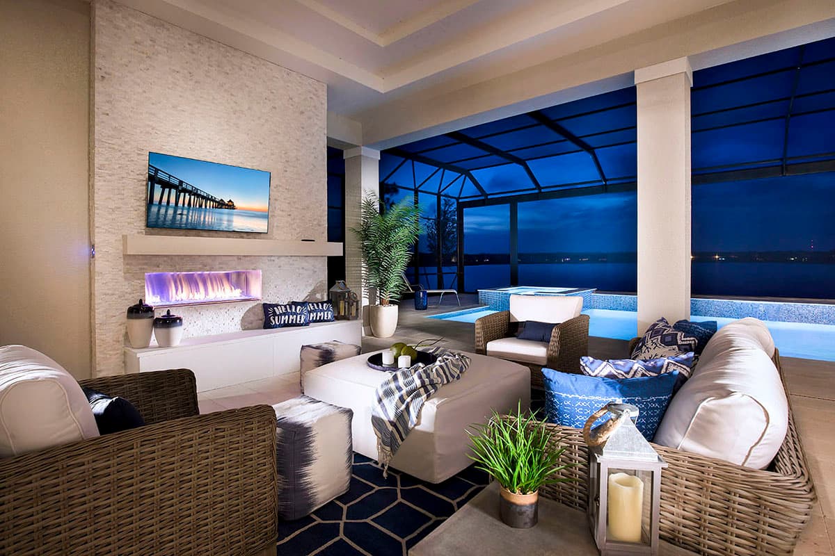 Covered patio with fireplace, seating, and pool overlooking water at dusk.