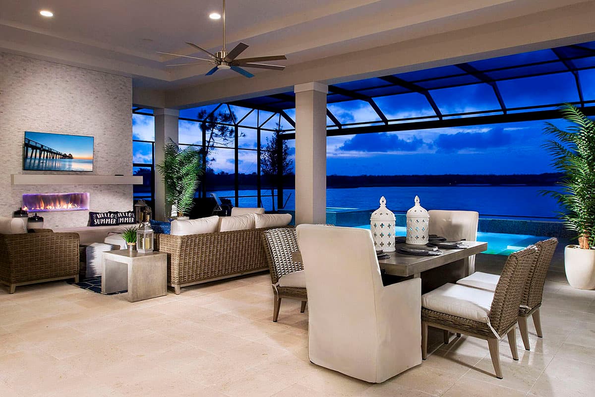 Covered outdoor living space with fireplace, seating area, dining table, and pool view at dusk.