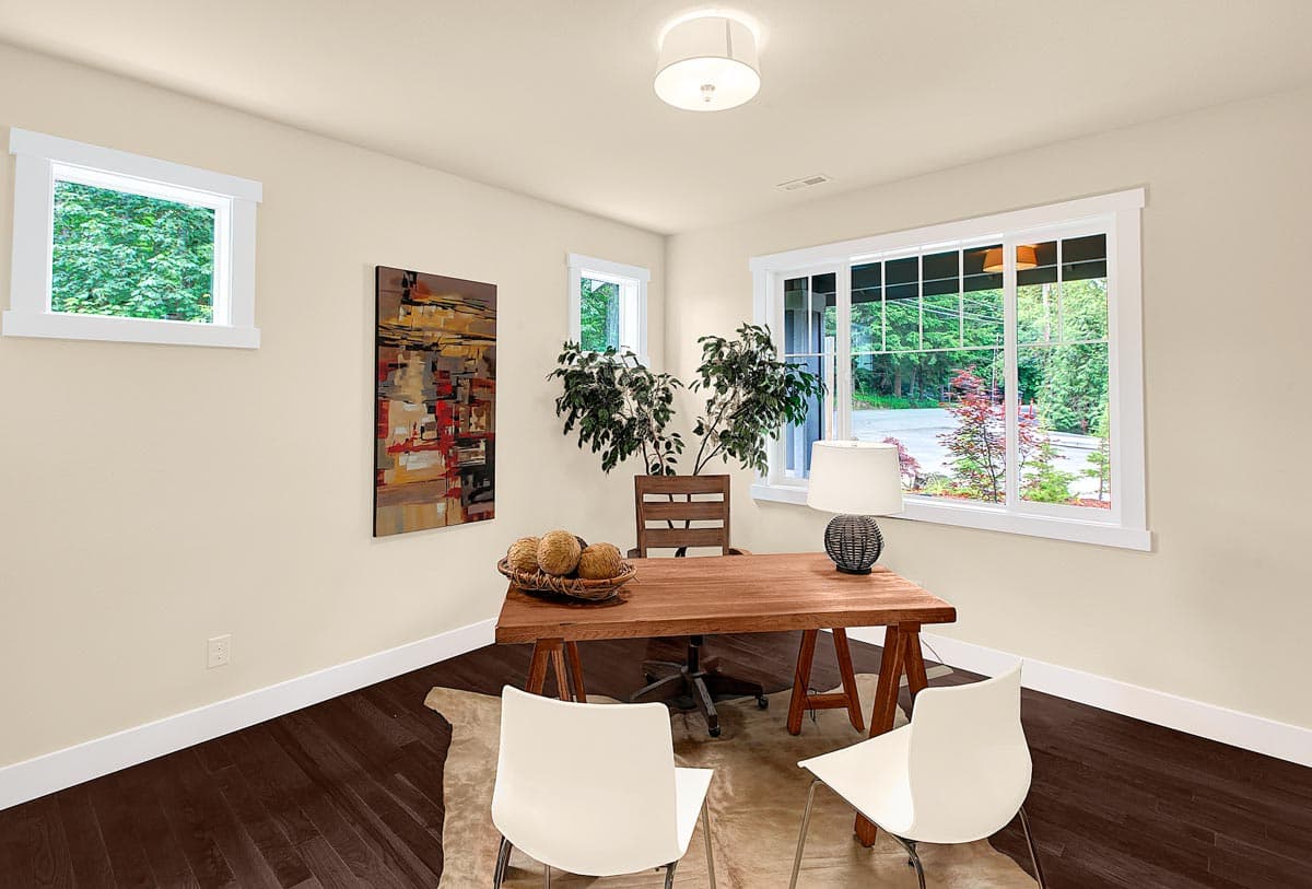Home office with a wooden desk, chairs, artwork, and large windows with forest views.