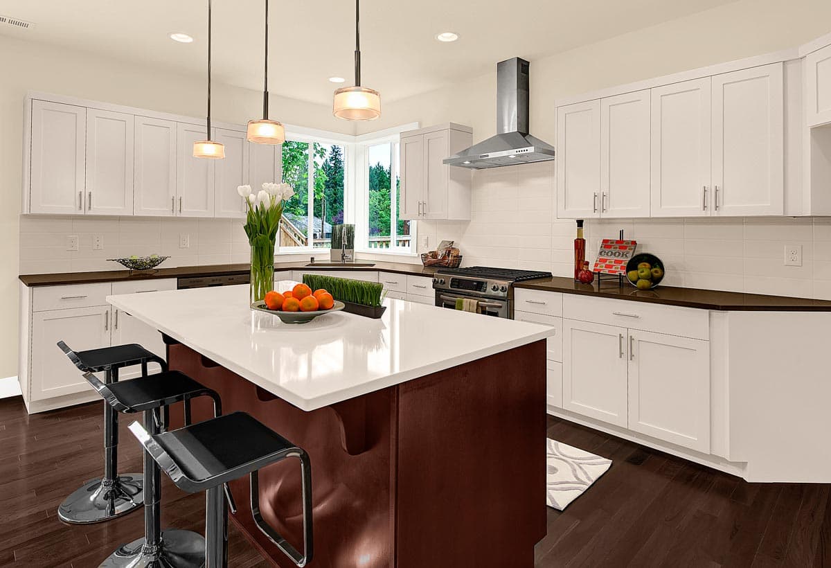 Modern kitchen with white shaker cabinets, dark wood floors, large island with seating, stainless steel range hood and backsplash.