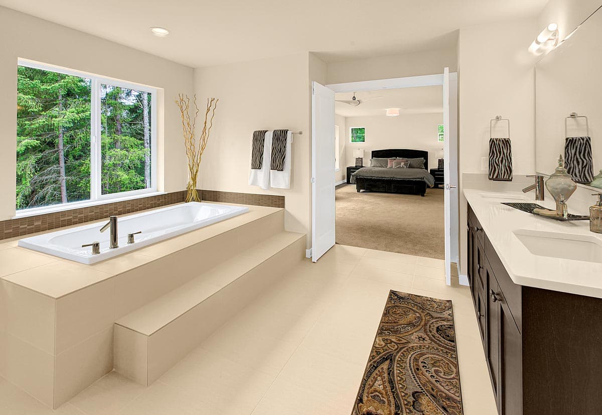 Master bathroom with large soaking tub and double vanity, opening to bedroom with king-size bed.