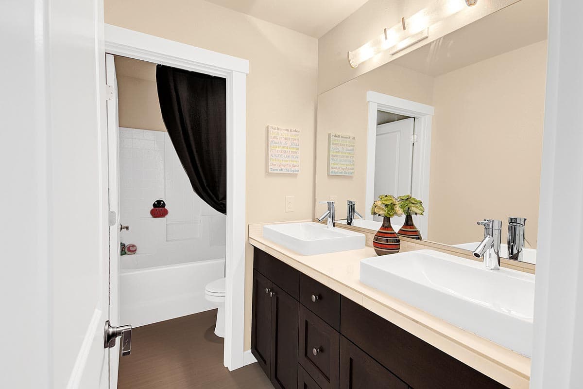 Bathroom with double vanity, vessel sinks, dark wood cabinets, and view into tub/shower area with black curtain.