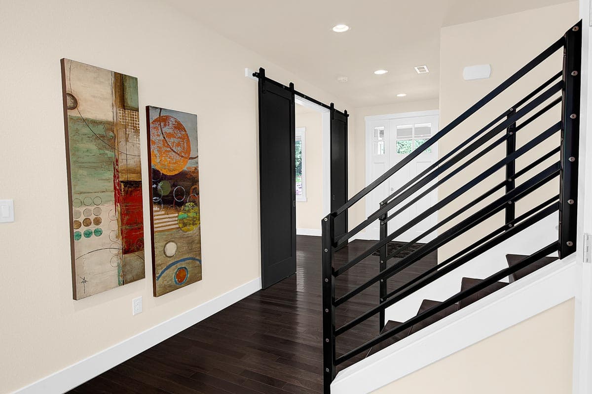 Interior view of hallway with dark wood floors, black barn door, contemporary metal staircase railing, and modern art.