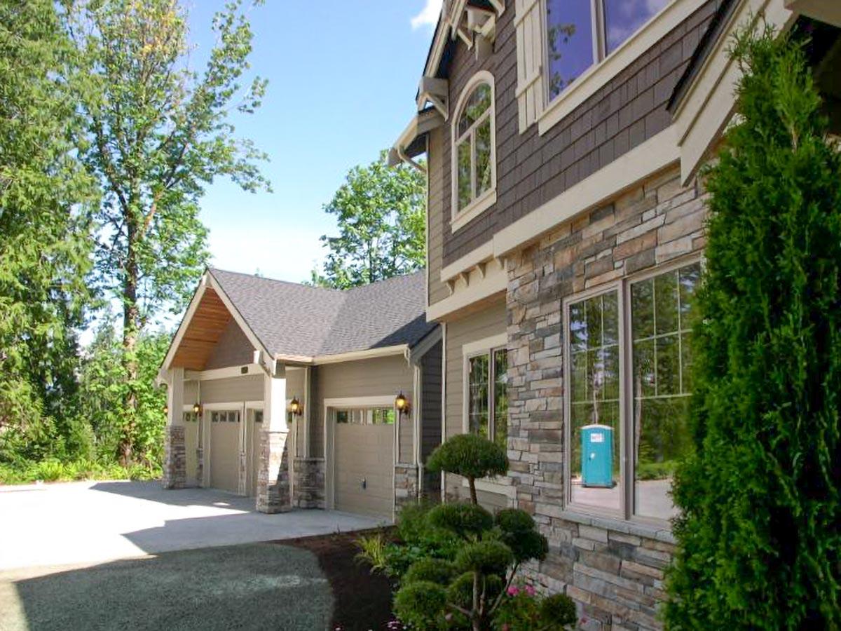 House plan exterior showing a two-story home with a three-car garage, stone facade, and arched window.