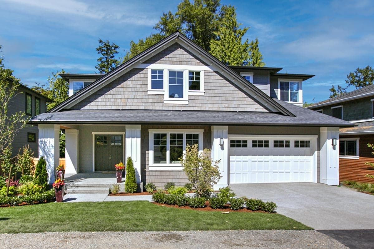 House plan exterior. Two-story Craftsman home with a gabled roof, front porch, and attached garage. Includes dormers and shake siding.