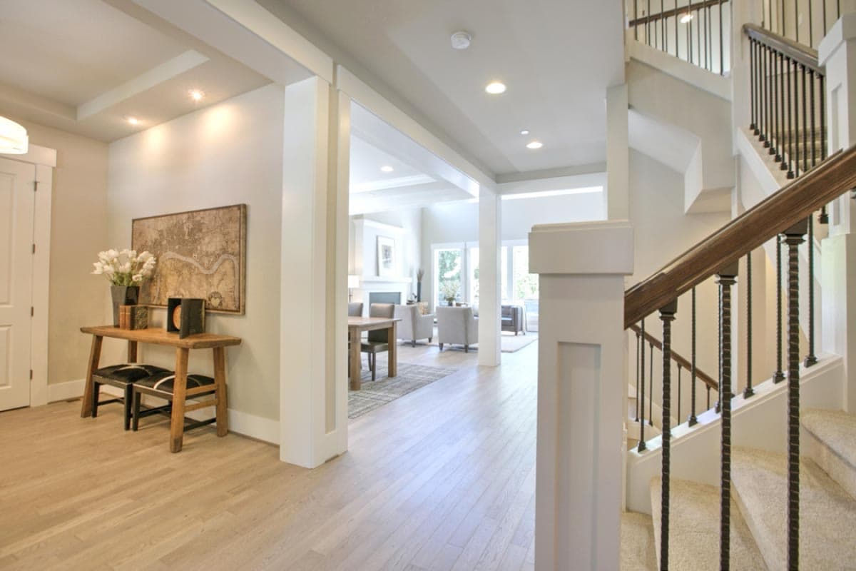 Interior view of house plan showing foyer with wood floor, staircase with metal spindles, and open doorway to living and dining areas.