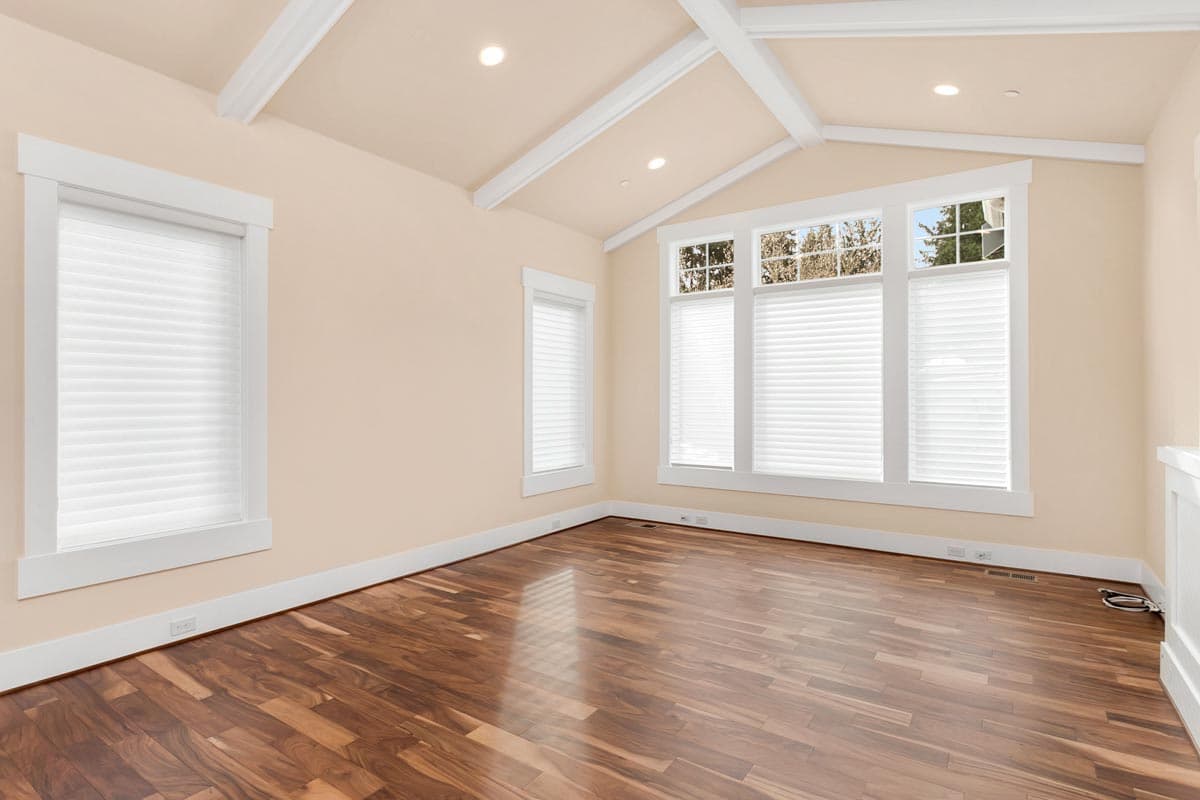 Interior view of an empty room with vaulted ceilings, exposed beams, hardwood floors, and large windows.