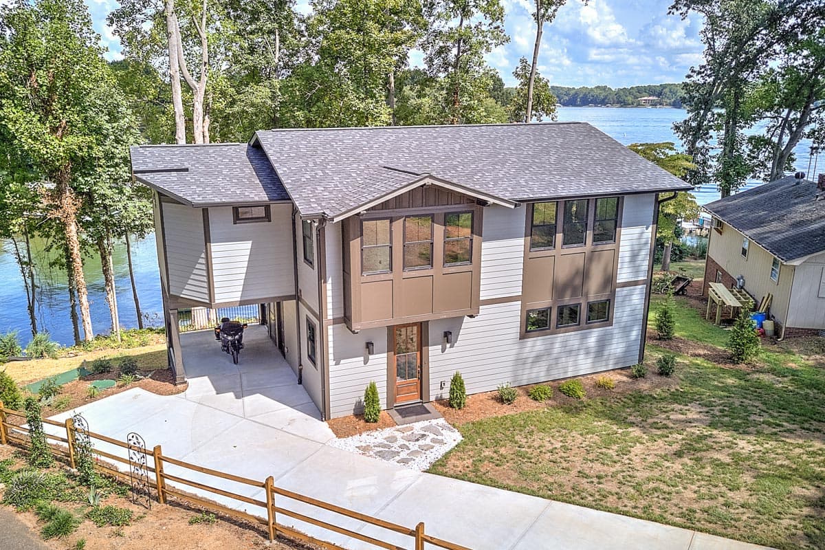 Modern house plan exterior with gabled dormer, second-story bay windows, and covered carport. Two stories, light siding, dark trim.