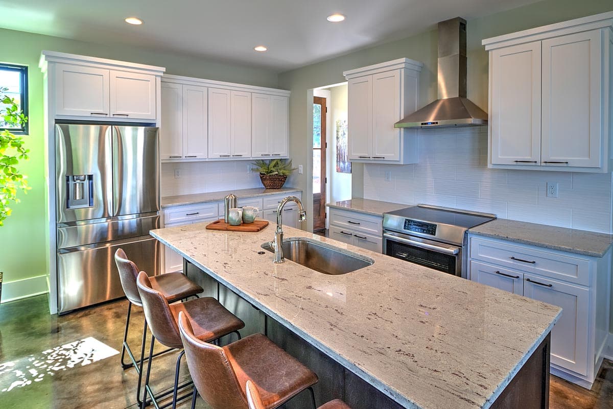 Kitchen with white shaker cabinets, granite island with sink, stainless steel appliances, and subway tile backsplash.