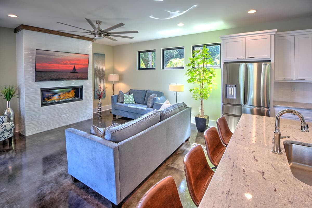 Interior view of living room with fireplace, television, seating, kitchen cabinets, refrigerator, and island.