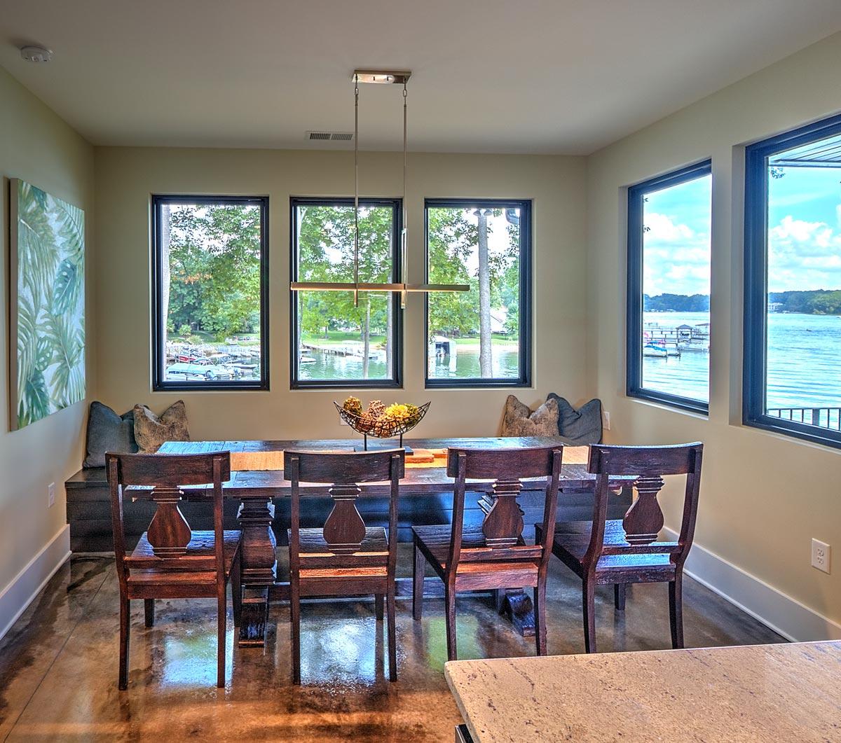Dining room with large windows overlooking a lake, dark wood dining set, and built-in bench seating.