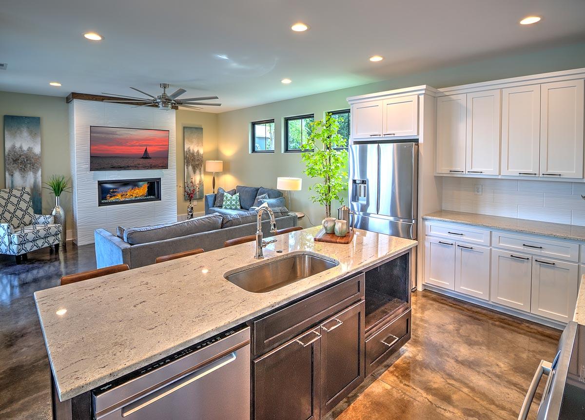 Open-concept living area with kitchen island, fireplace, sectional sofa, and stainless steel appliances.